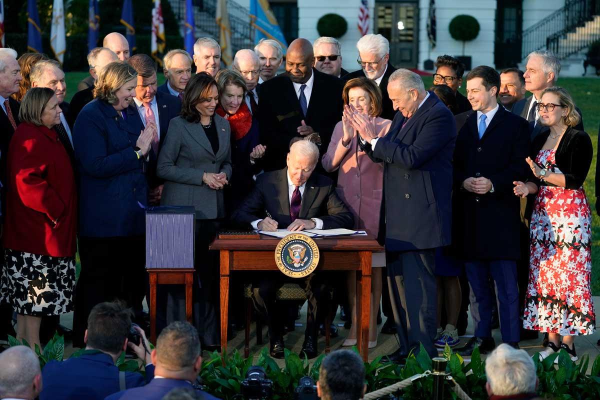 President Joe Biden signing a document surrounded by a group of people, including Vice President Kamala Harris, lawmakers, and officials, outside the White House