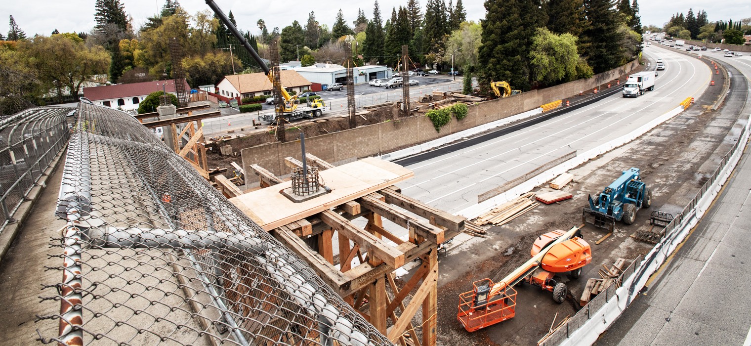 Construction of a highway improvment project, with heavy machinery, scaffolding, and workers visible.